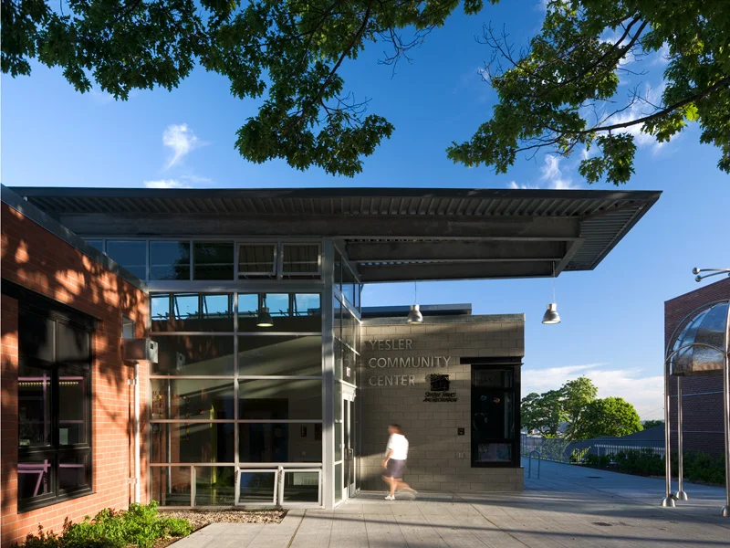 Exterior approach to a community center with brick facade, large glazed entrance lobby, and deep overhanging canopy by Mithun.