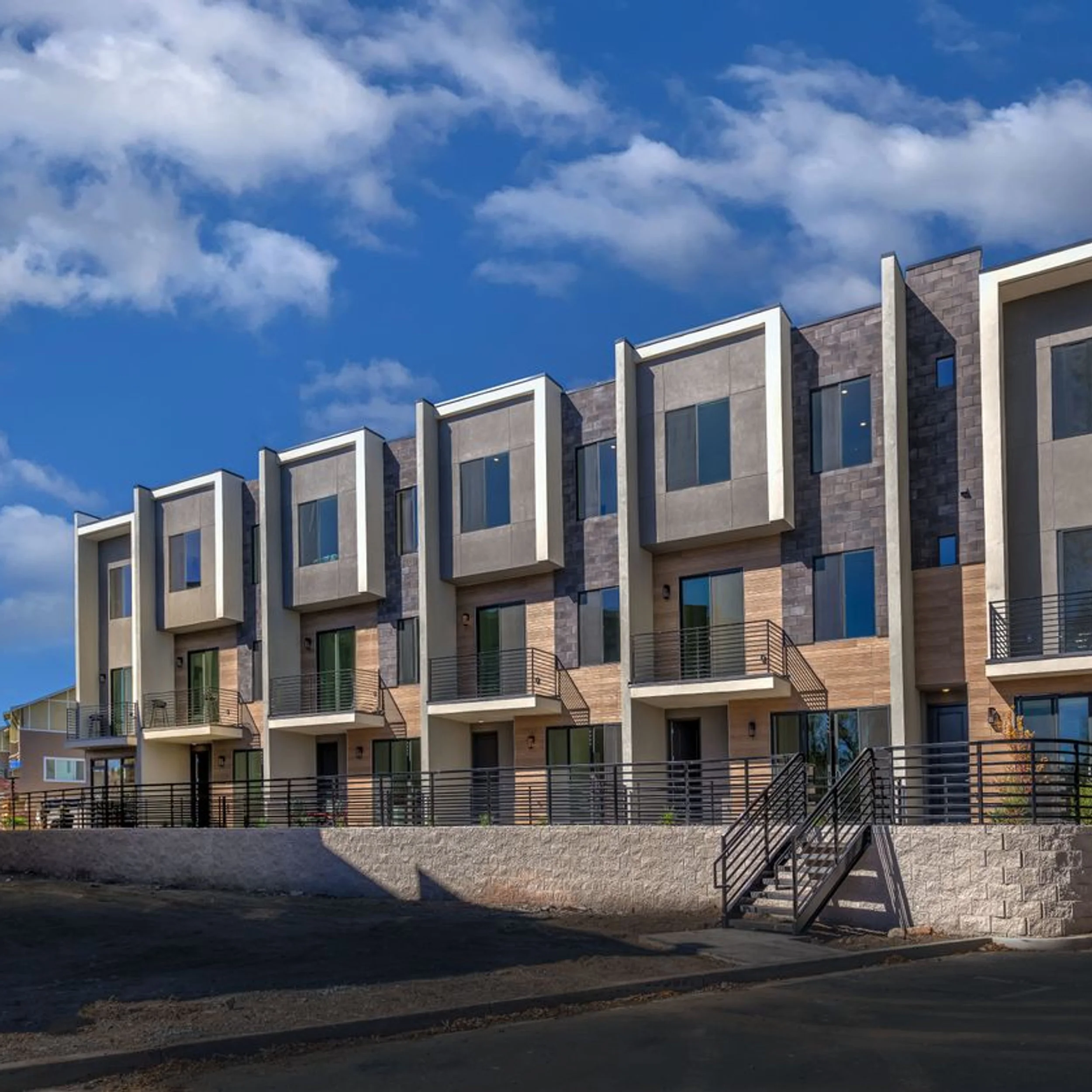 Exterior facade of TRUCKEE RIVER GREEN by Frame Architecture, Inc, featuring stepped townhome volumes with concrete frames and dark paneling.