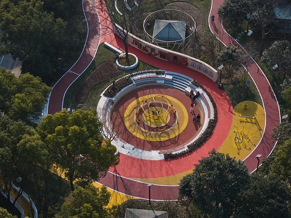 Aerial view of a circular pocket park in Shanghai with concentric colored running tracks and a central playground climbing structure.