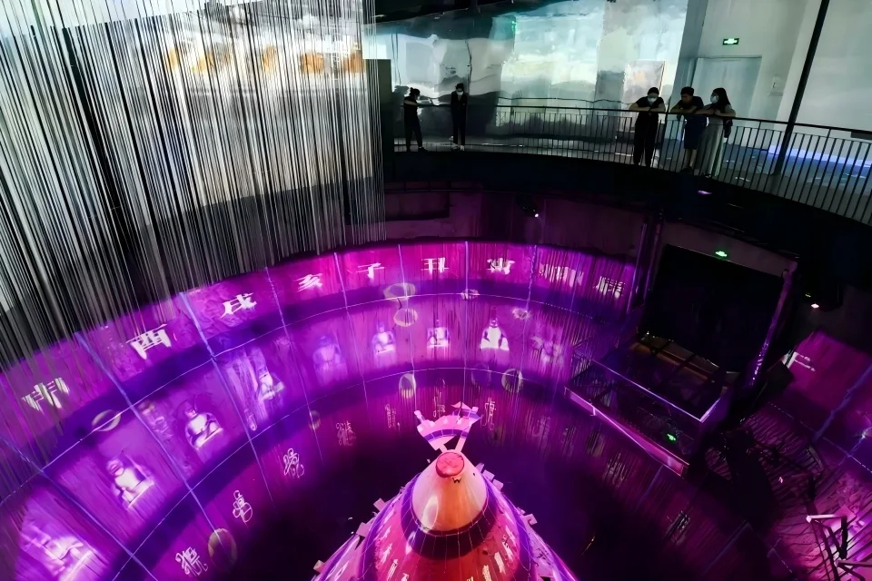 Interior view from above of a circular multi-level exhibition hall with projected light displays and visitors on an upper balcony by 清城睿现公司.