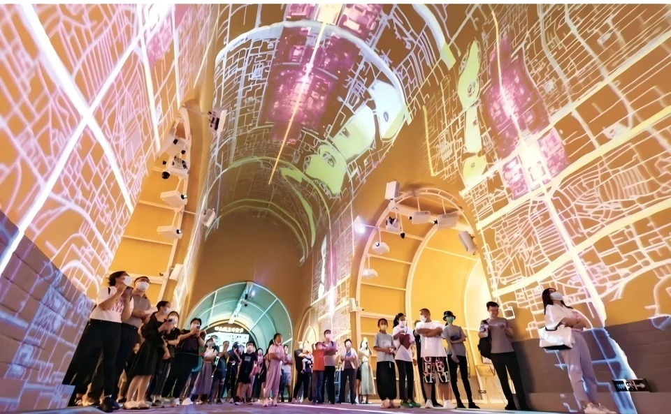 Vaulted exhibition hall interior featuring large-scale digital projection mapping on curved walls and ceiling, with visitors looking up.