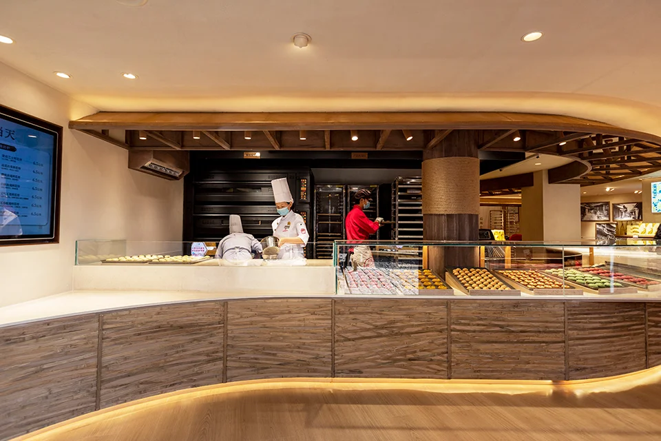 Curved bakery counter with textured wood panels and glass display cases by Yuhi Studio.