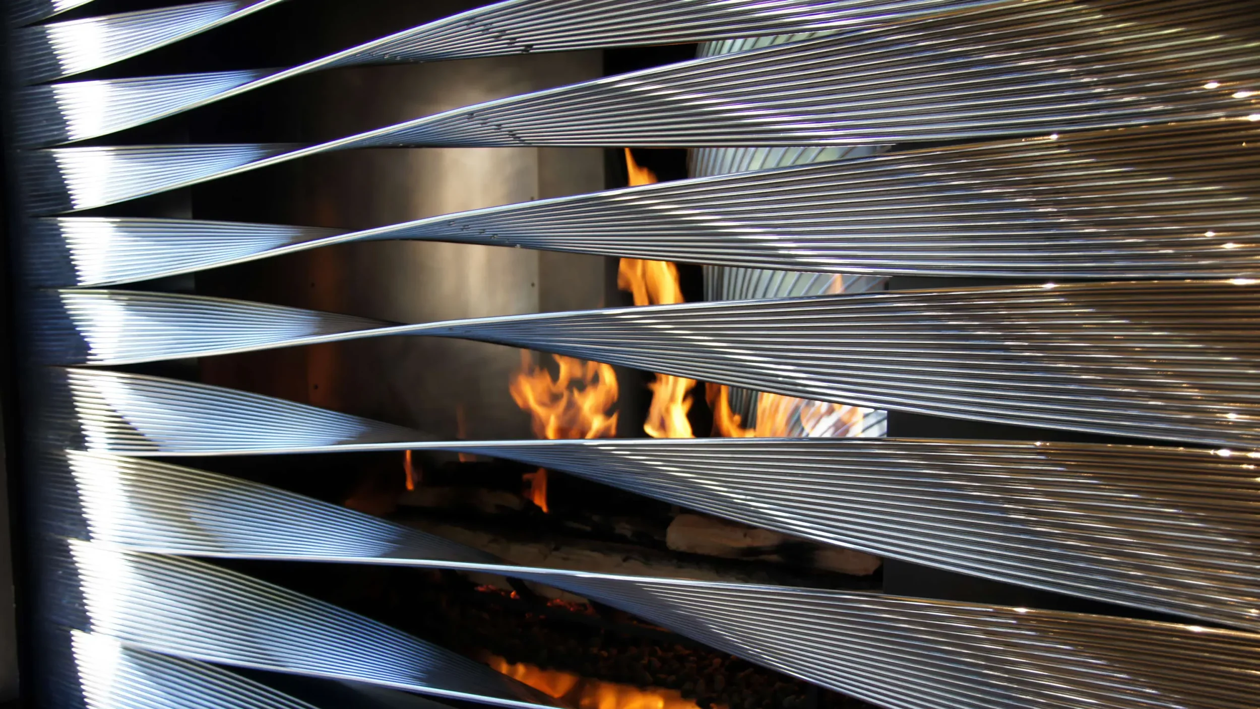 Close-up of Ron Arad Studio fireplace screen featuring twisted polished metal fins revealing flames behind.