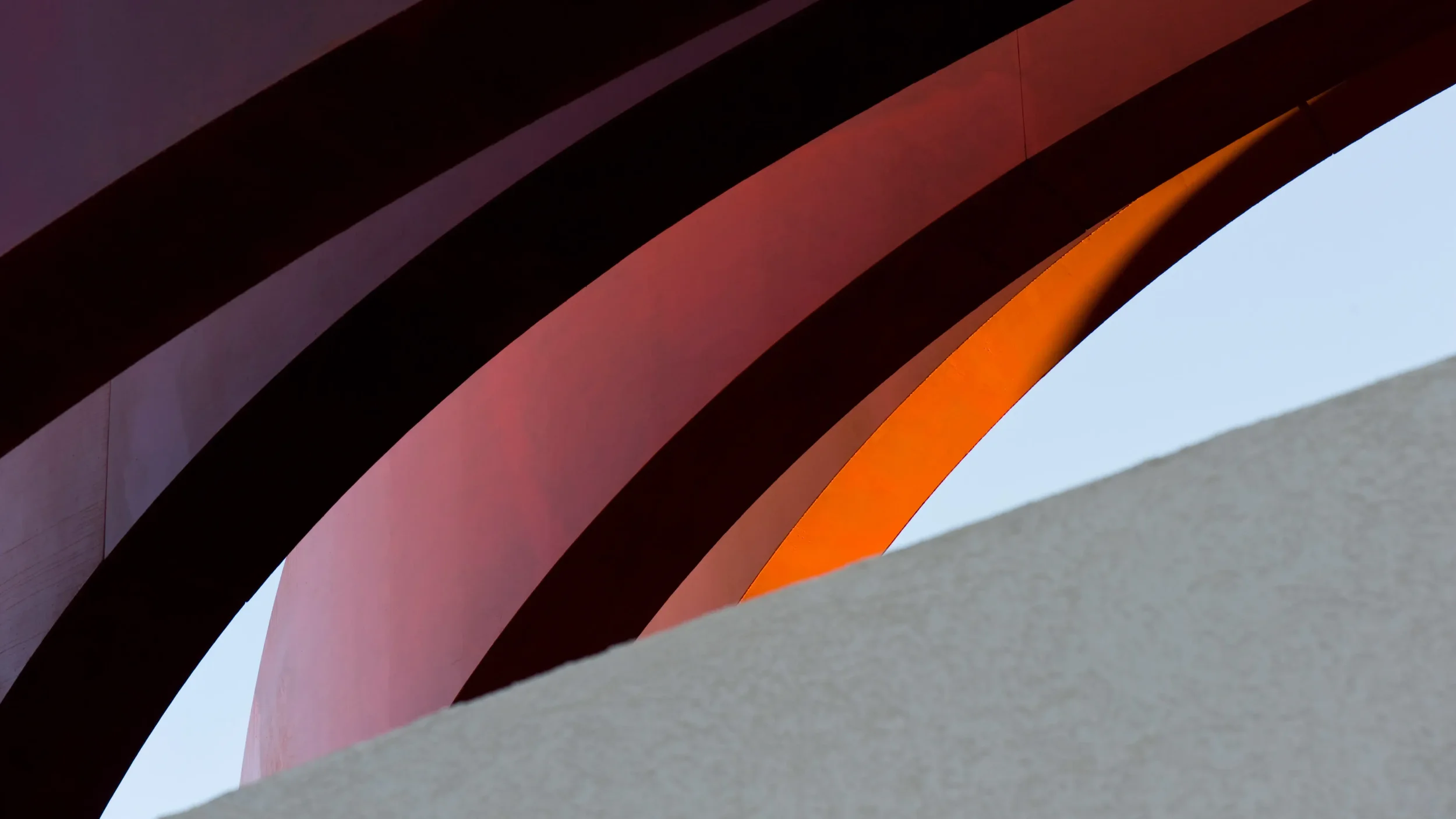 Curved red metallic structural elements overlapping against a pale background by Ron Arad Studio.