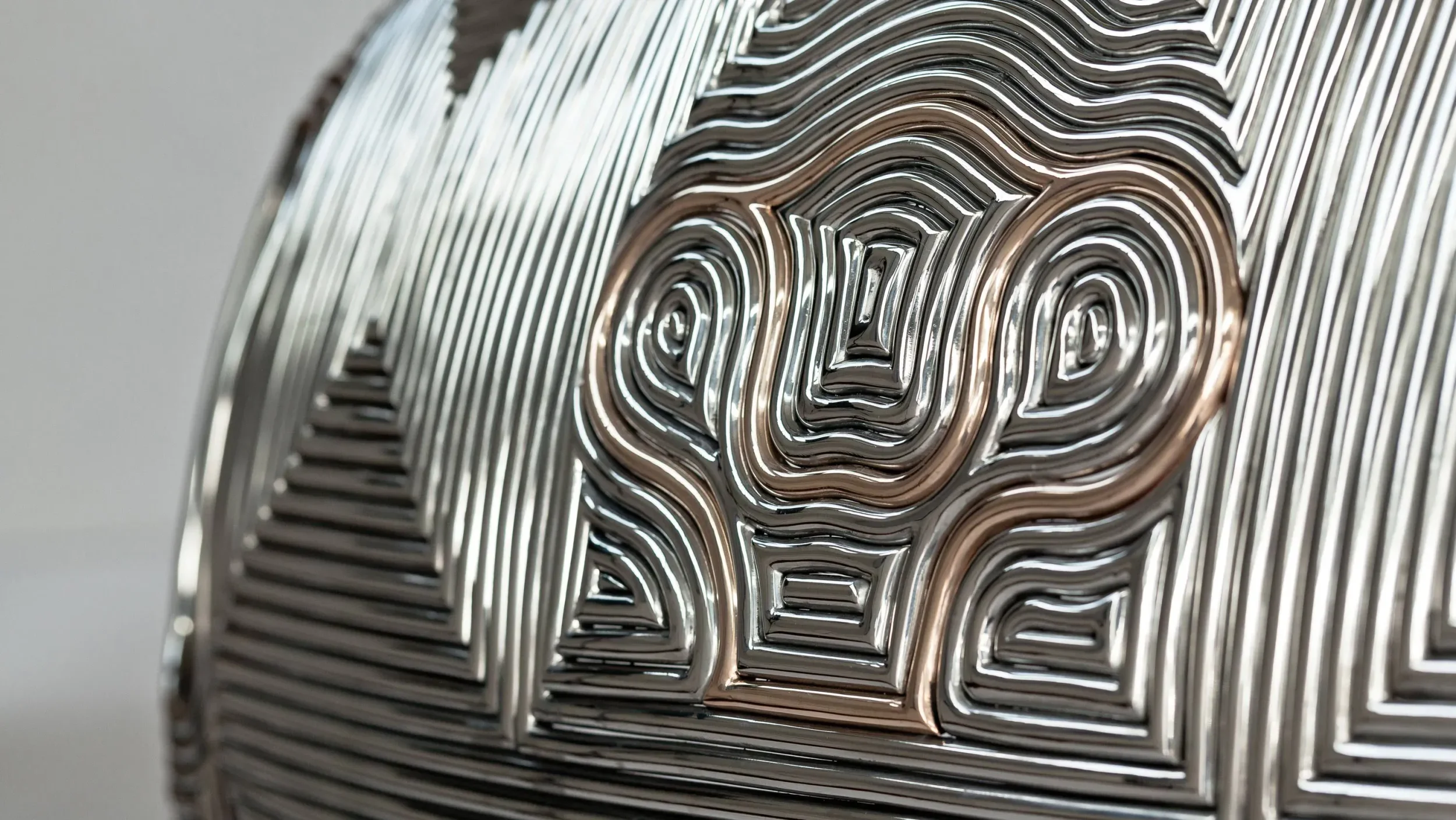 Close-up of polished curved metal object with CNC-milled topographic relief patterns by Ron Arad Studio.