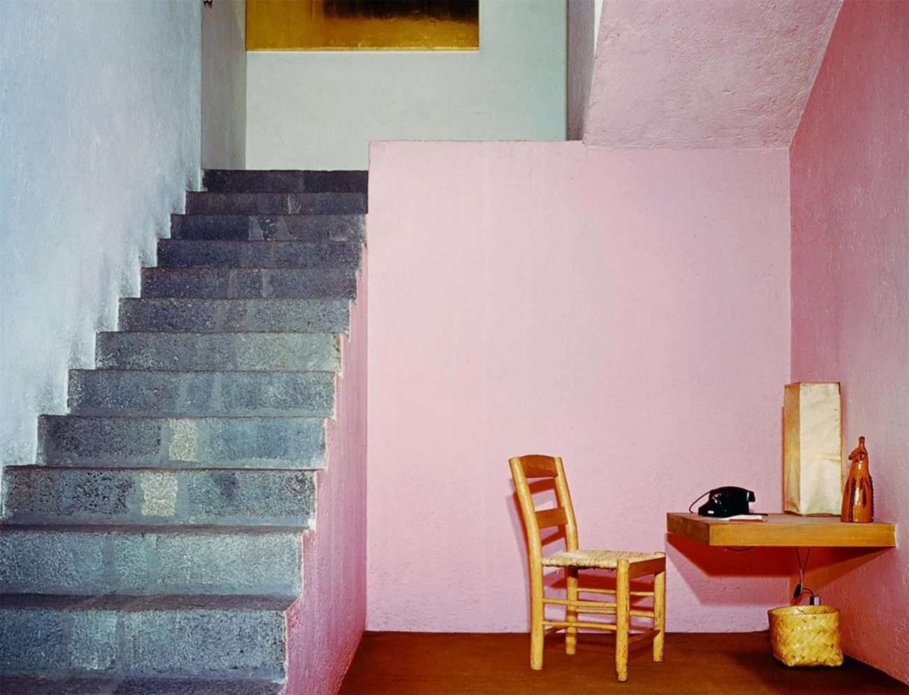 Interior of Barragán House showing volcanic stone stairs next to a pink wall with a wooden chair and desk.