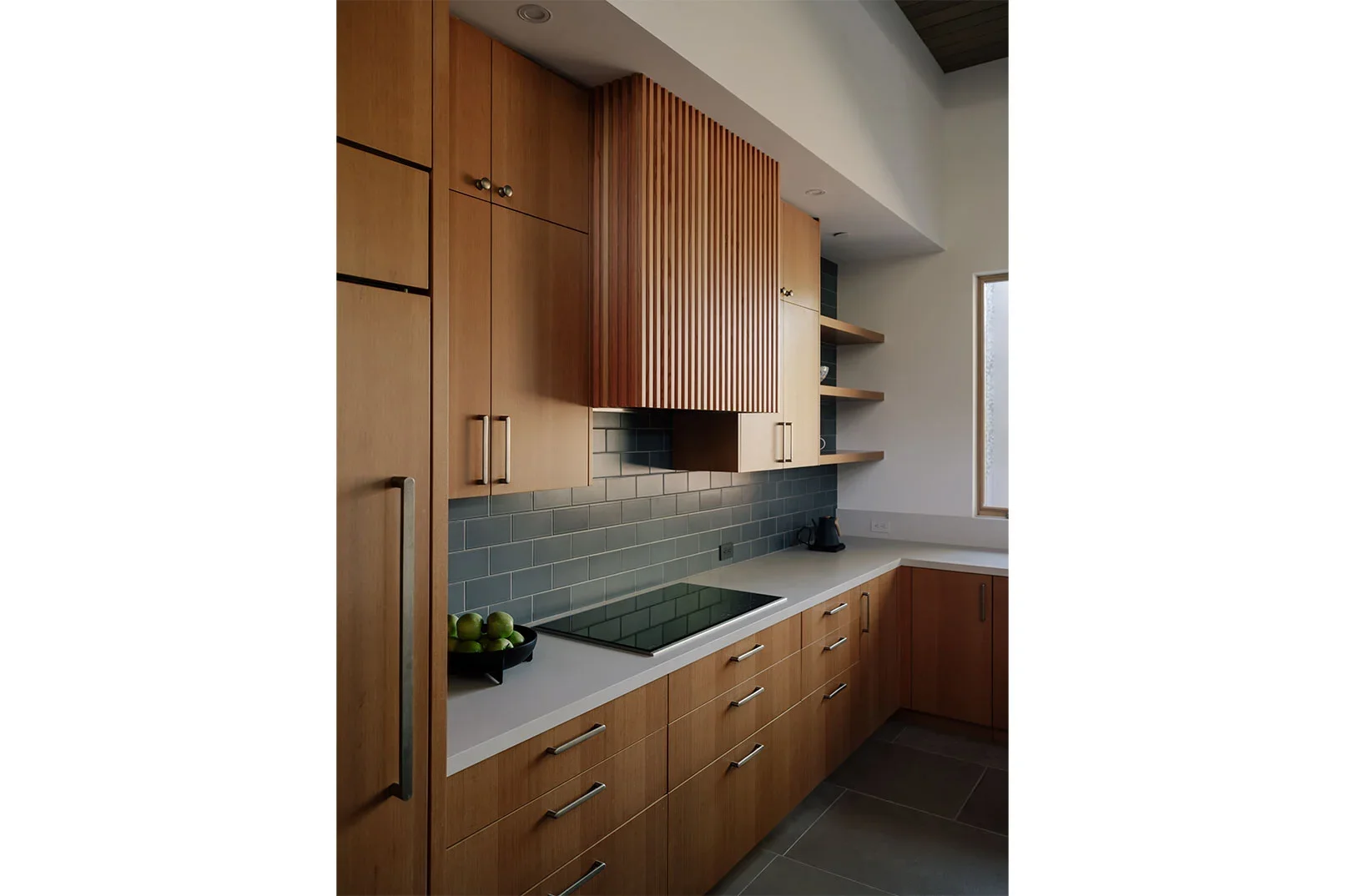 Contemporary kitchen by Ana Williamson Architect featuring warm wood cabinetry, a slatted range hood, and dark grey tile backsplash.