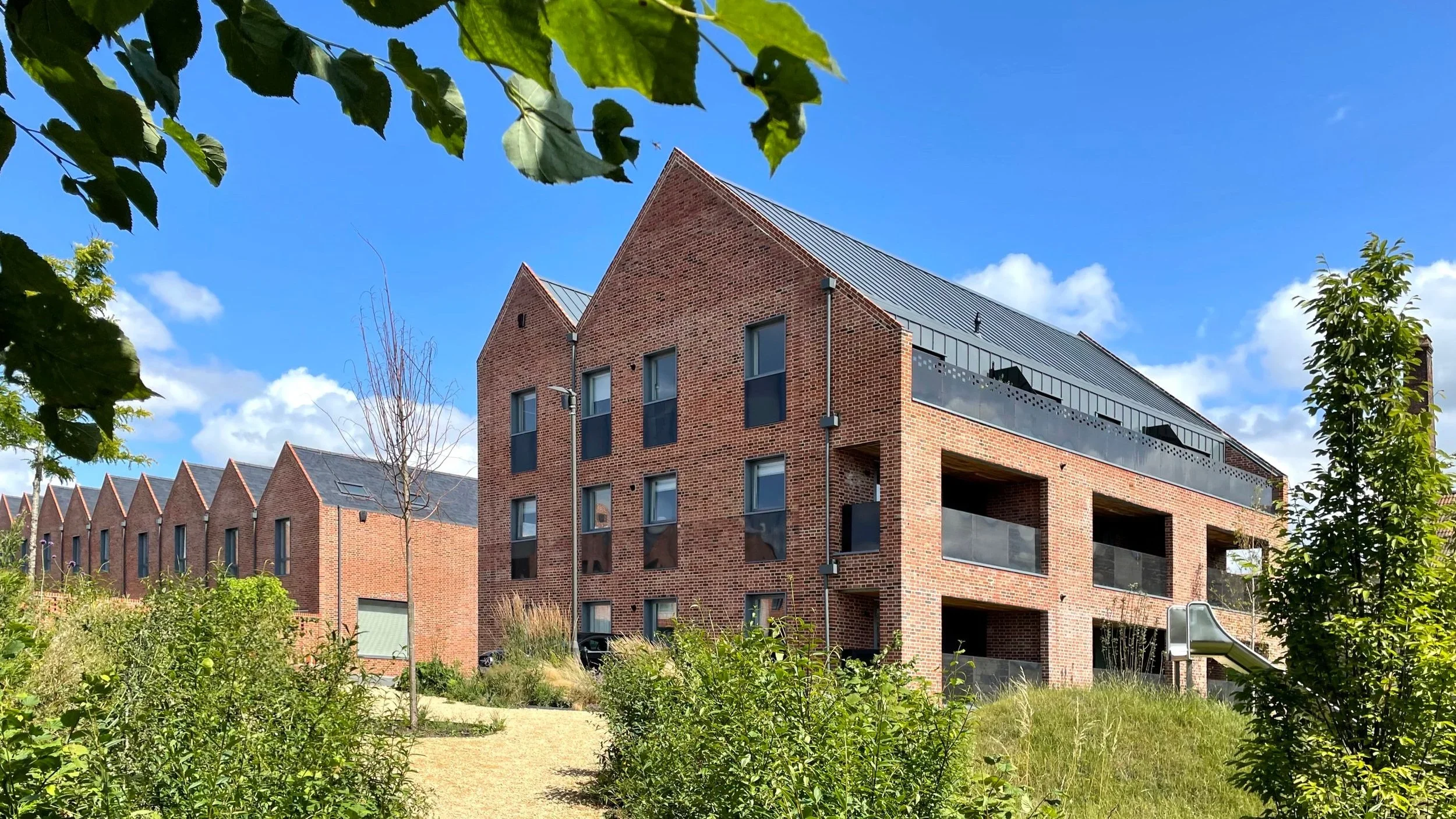 Exterior view of brick housing blocks with pitched roofs and recessed balconies by Mitchell Eley Gould in Bath.