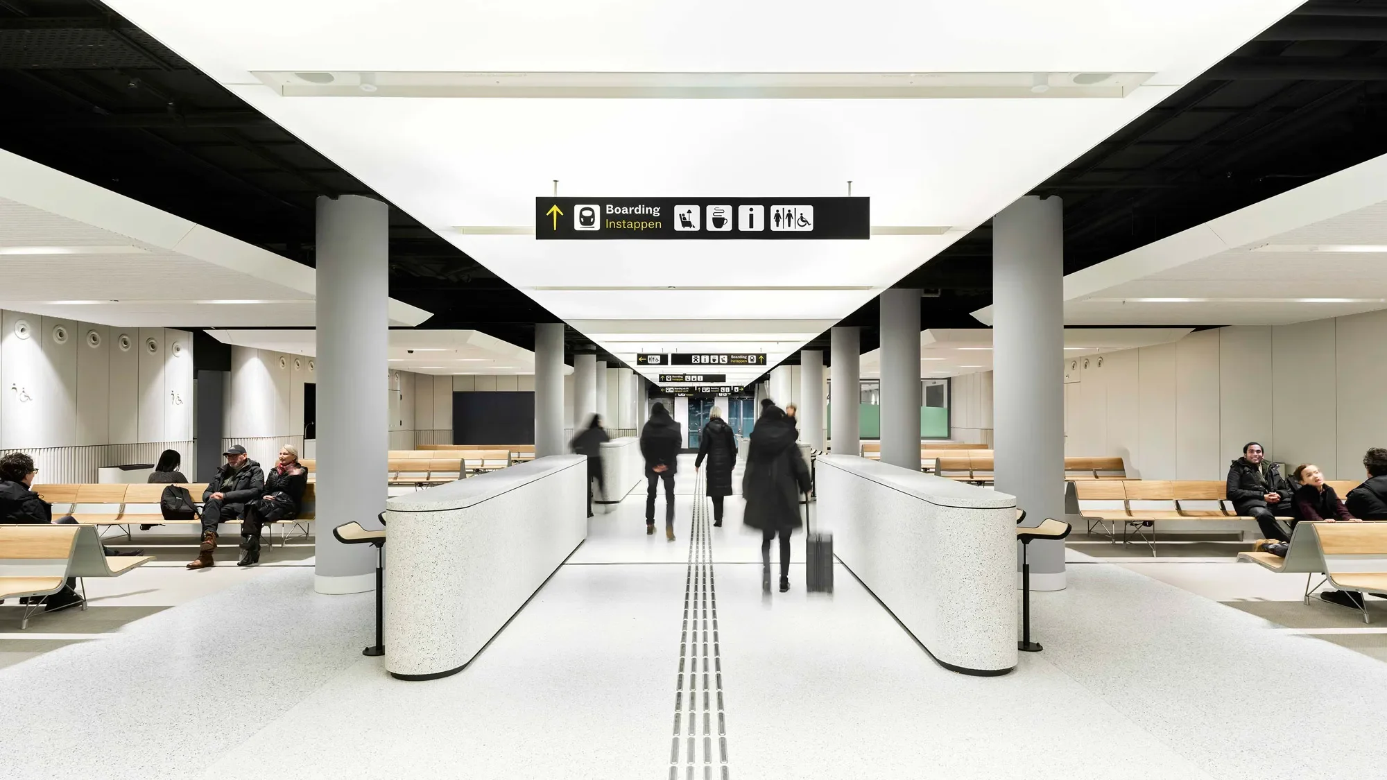 Interior of Eurostar UK Terminal in Amsterdam by Superimpose Architecture showing a bright transit concourse with terrazzo floors, curved barriers, and integrated luminous ceiling panels.