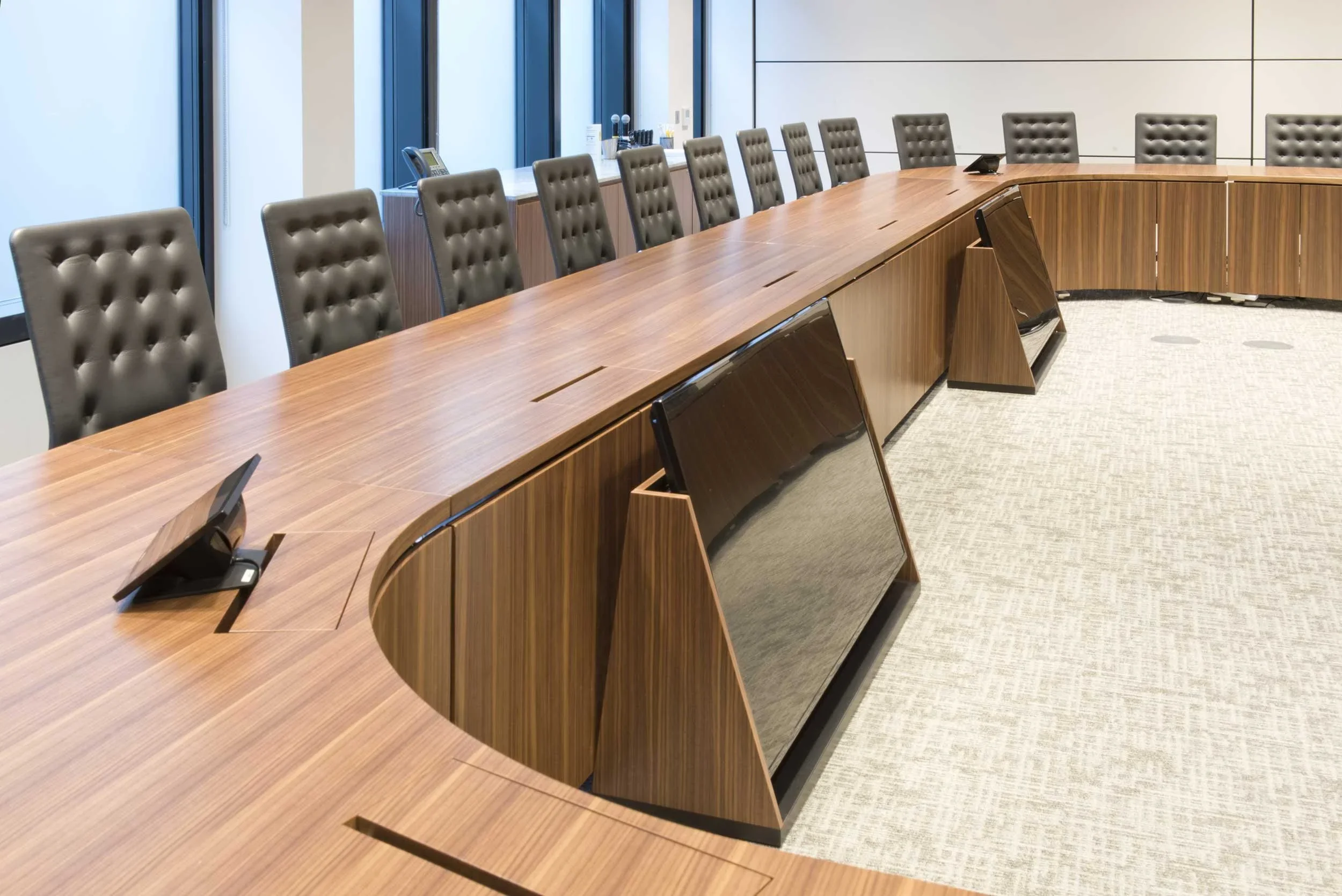 Curved custom wooden conference table with integrated audio-visual technology and tufted leather chairs in a Canary Wharf office interior by Opus Magnum.