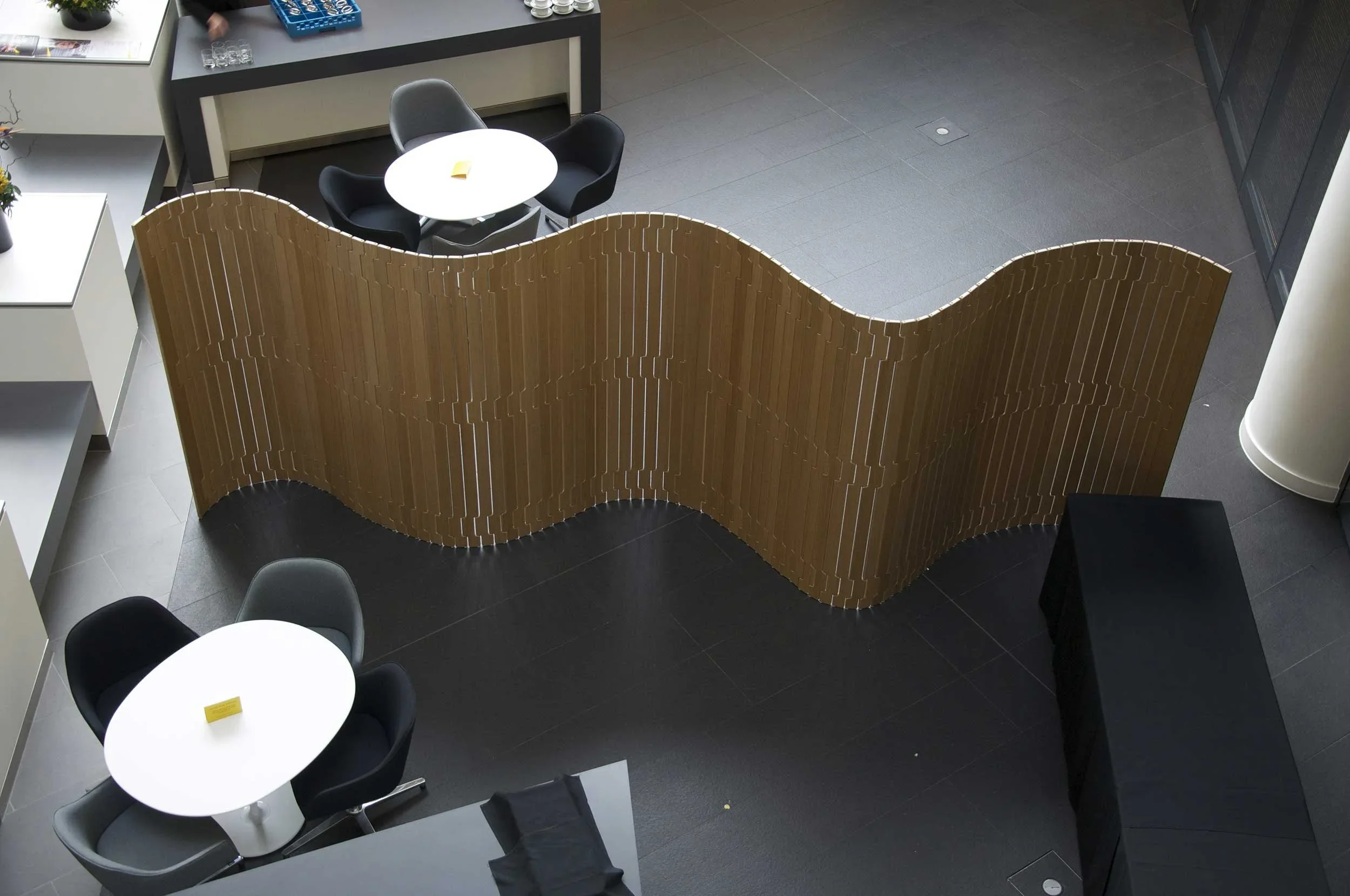 High-angle interior view of an open office floor with a sinuous slatted timber divider screen by Opus Magnum.