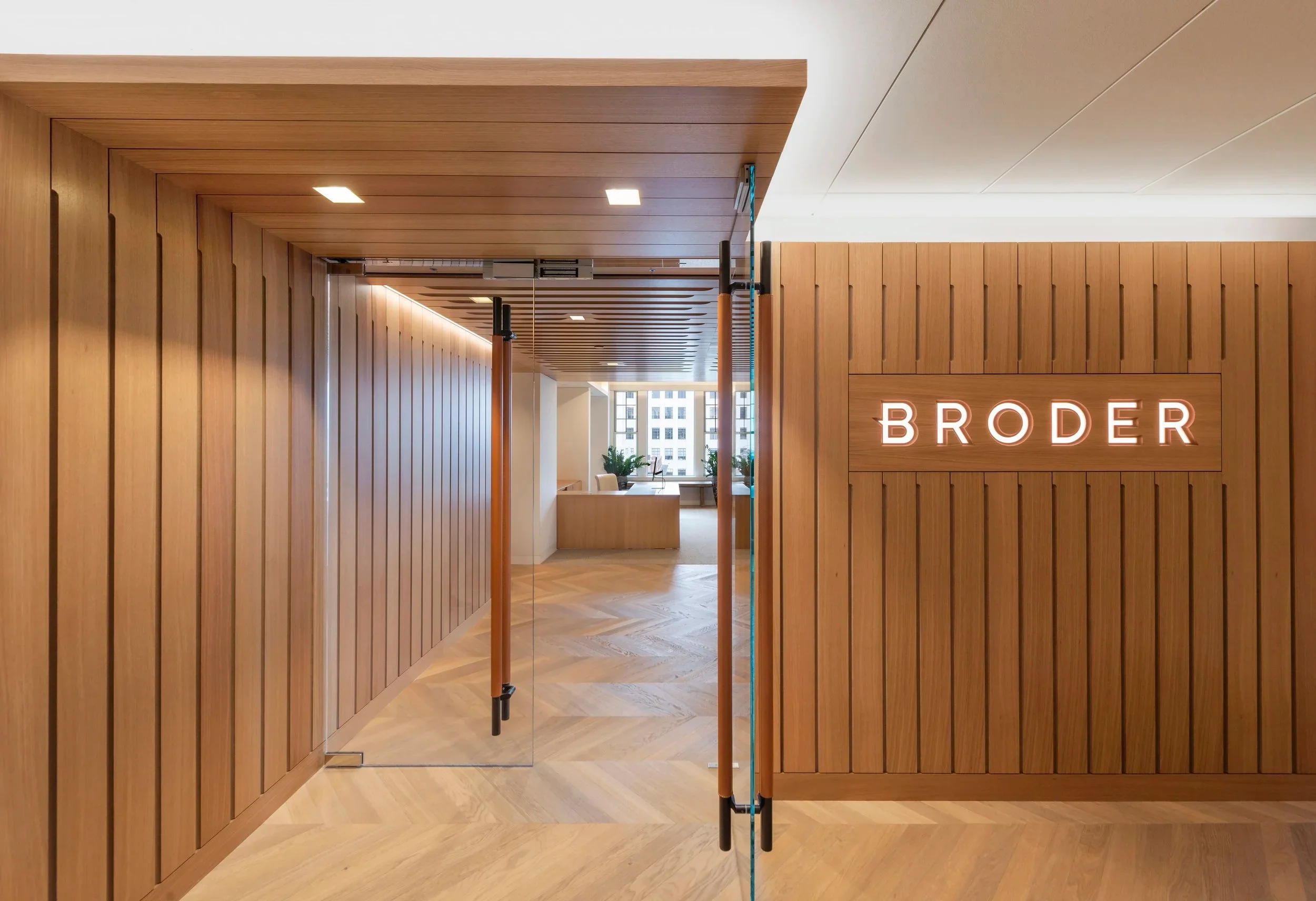 Corporate office entrance with custom vertical timber slat paneling, herringbone wood flooring, and illuminated signage by Touloukian Touloukian Inc.