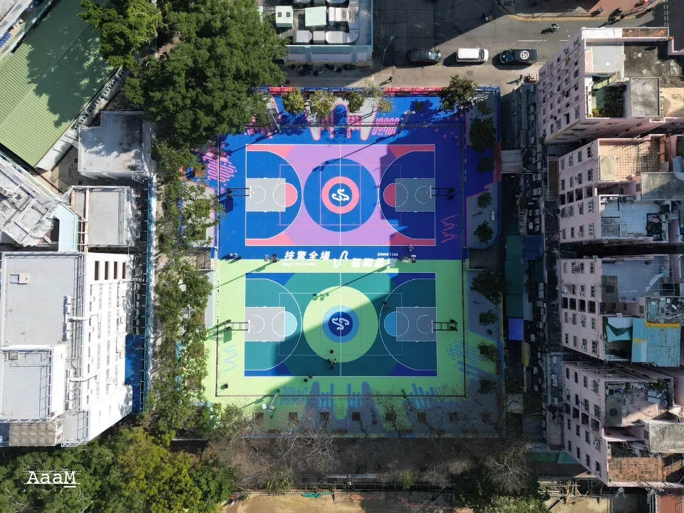 Aerial view of a brightly painted blue and green outdoor basketball court in an urban setting by AaaM.