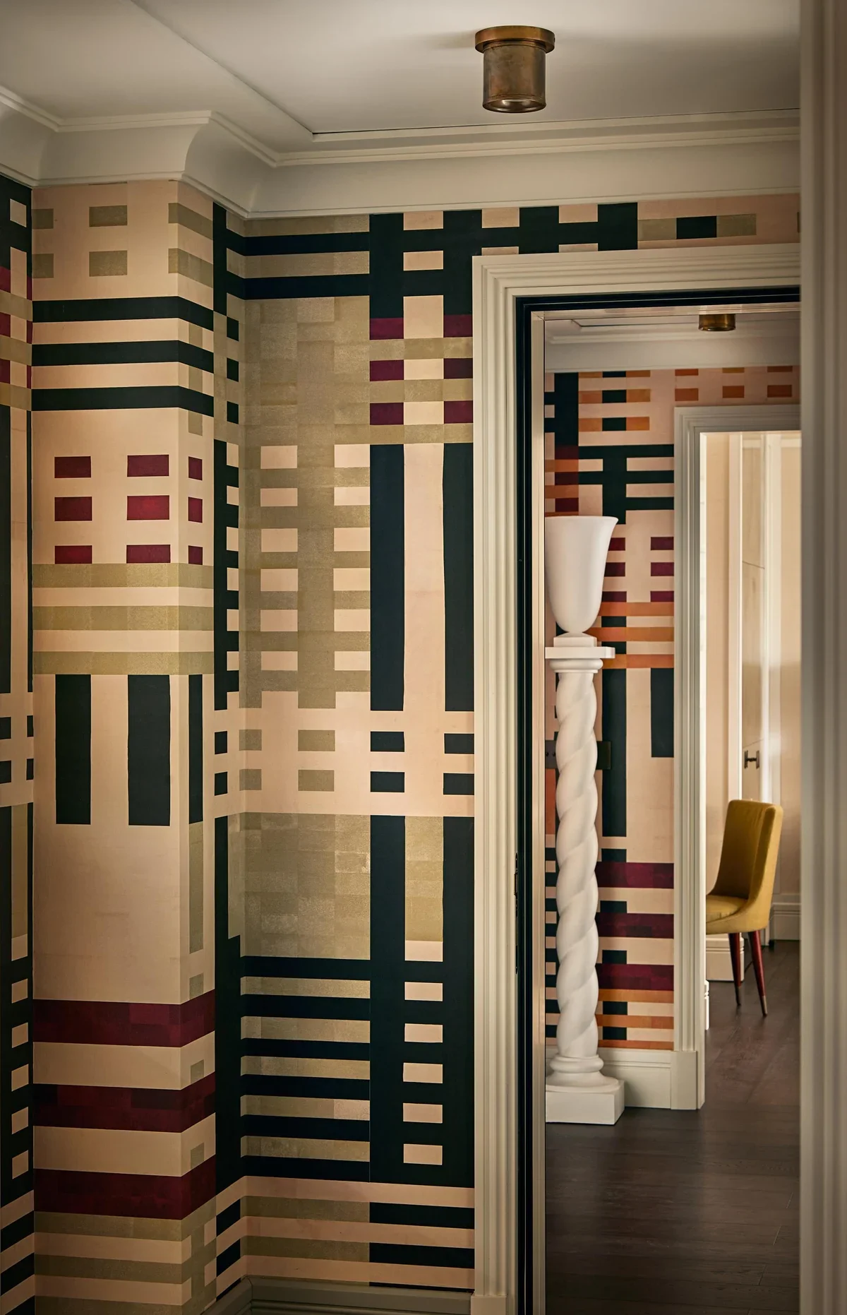 Interior hallway with geometric plaid wallpaper and nested doorways framing a twisted column by Paolo Moschino.