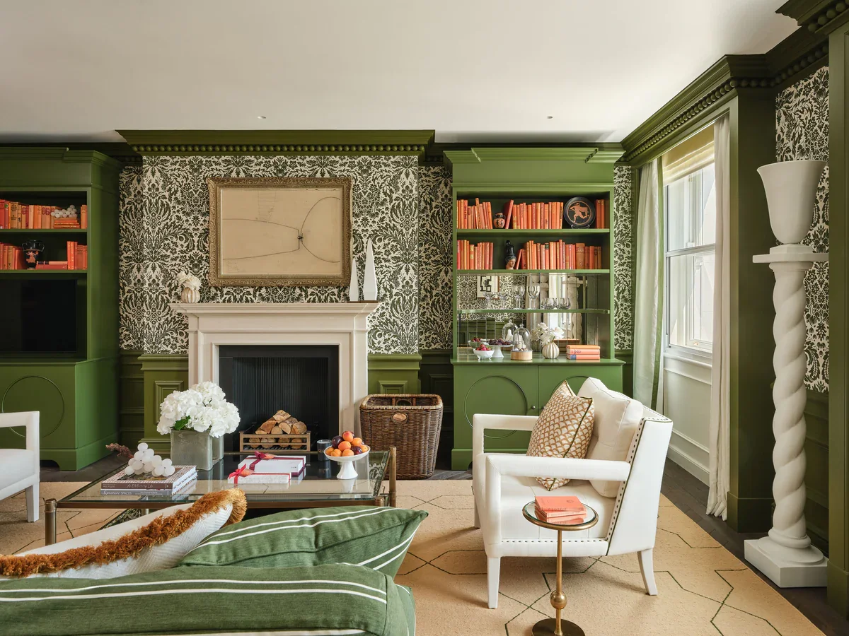 Living room interior by Paolo Moschino with olive green built-in cabinetry, patterned wallpaper, and a traditional fireplace.