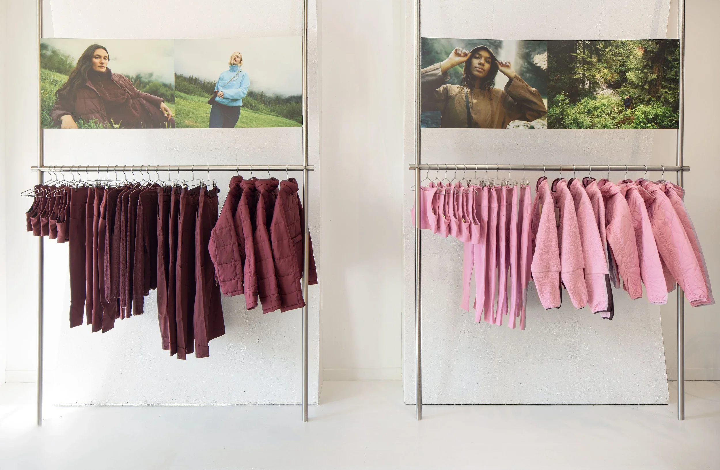 Retail interior display by Reflect Architecture featuring freestanding steel clothing racks with burgundy and pink garments beneath graphic lifestyle panels.